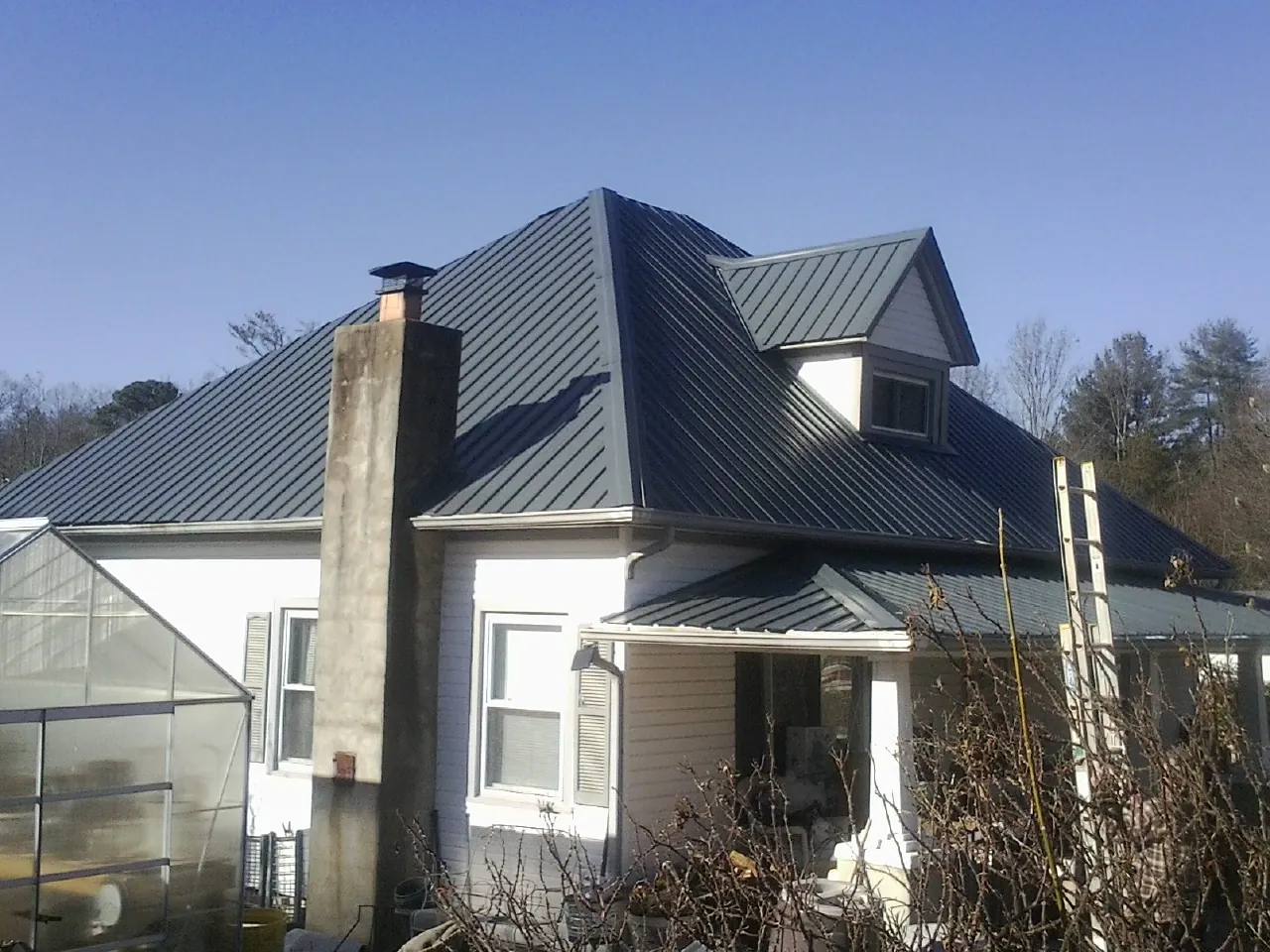 Dark blue standing seam metal roof on a white farmhouse with dormer — Slate & Tile Roof Repair by Roofing Brothers in Westfield Center