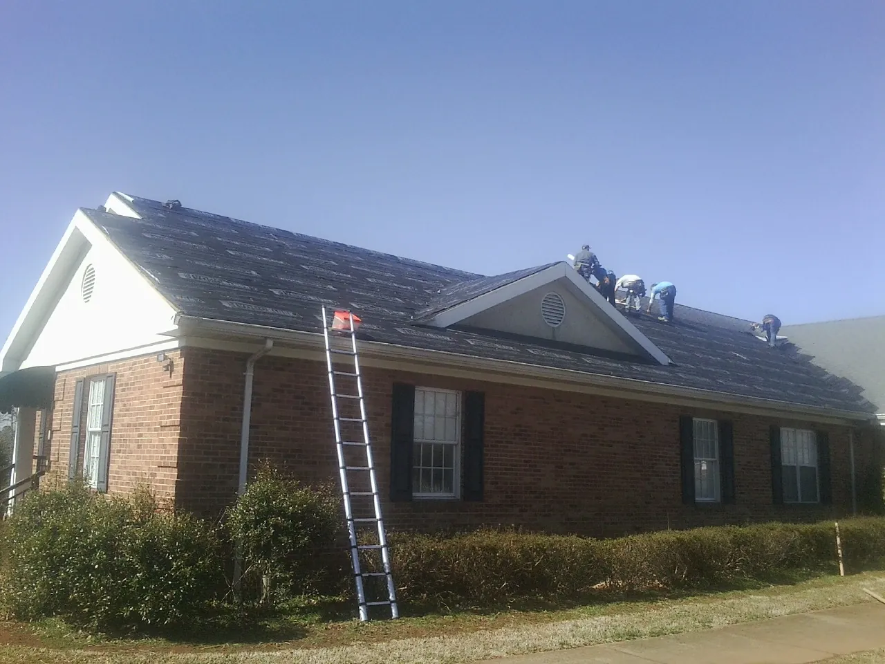 Crew tearing shingles off a brick ranch roof with a ladder set — Metal Roof Repair work by our crew in Westfield Center