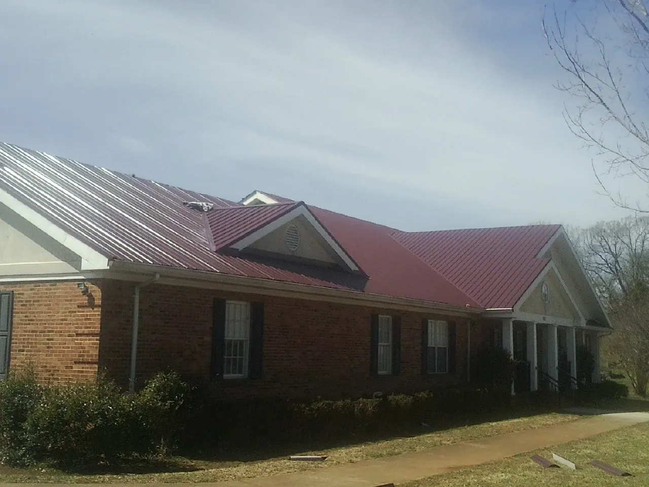 Red metal roof with gabled entries on a long brick building, from a Hail Damage Roof Repair job in Westfield Center