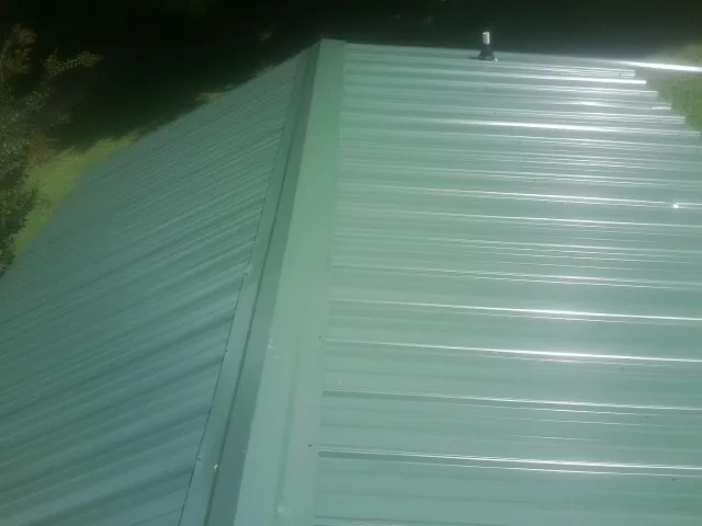 New green metal panels meeting at the ridge of a roof — Flat Roof Repair work by our crew in Westfield Center
