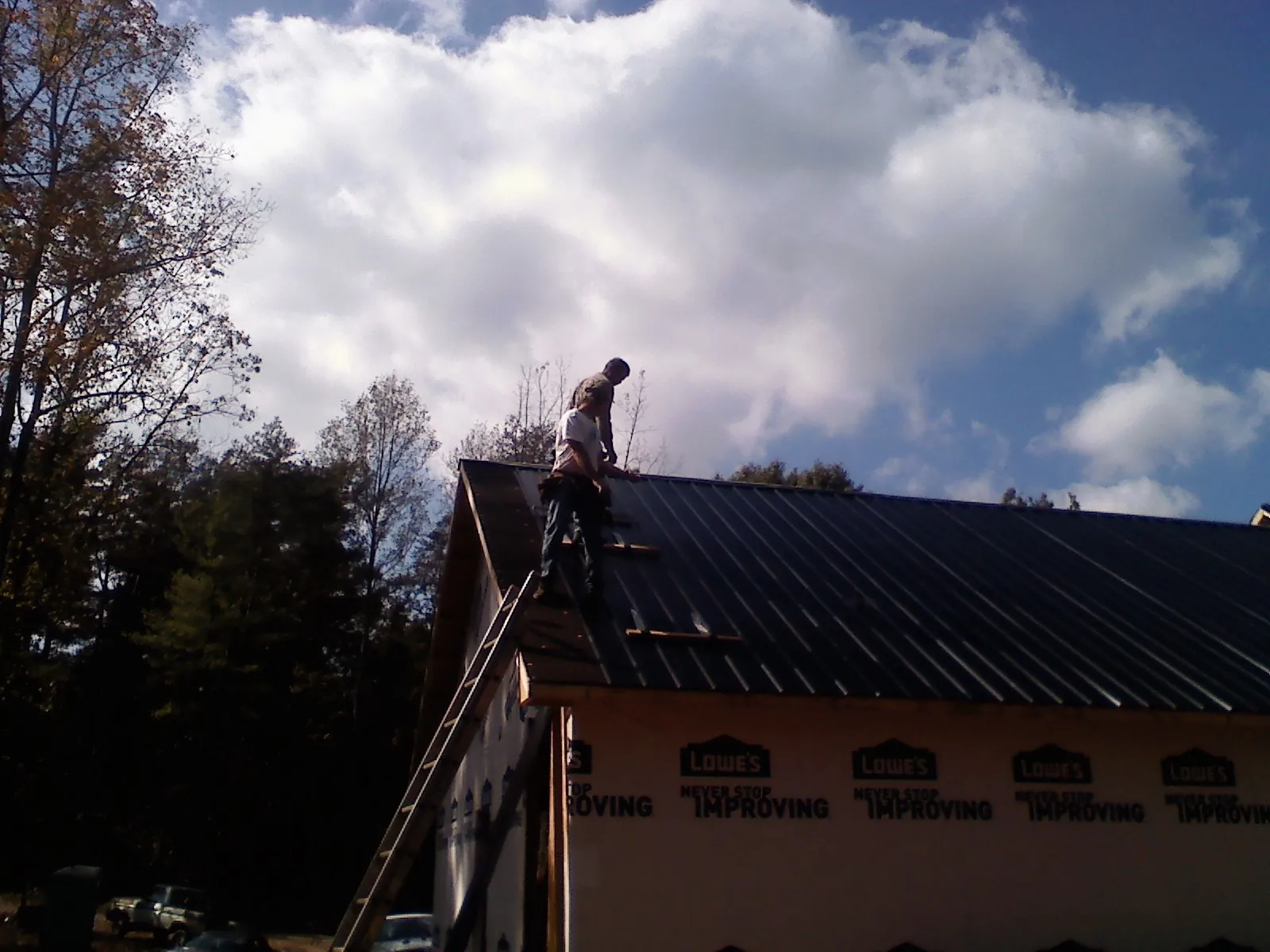 Roofer fastening dark metal panels high against a cloudy sky, from a Roof Inspection job in Westfield Center