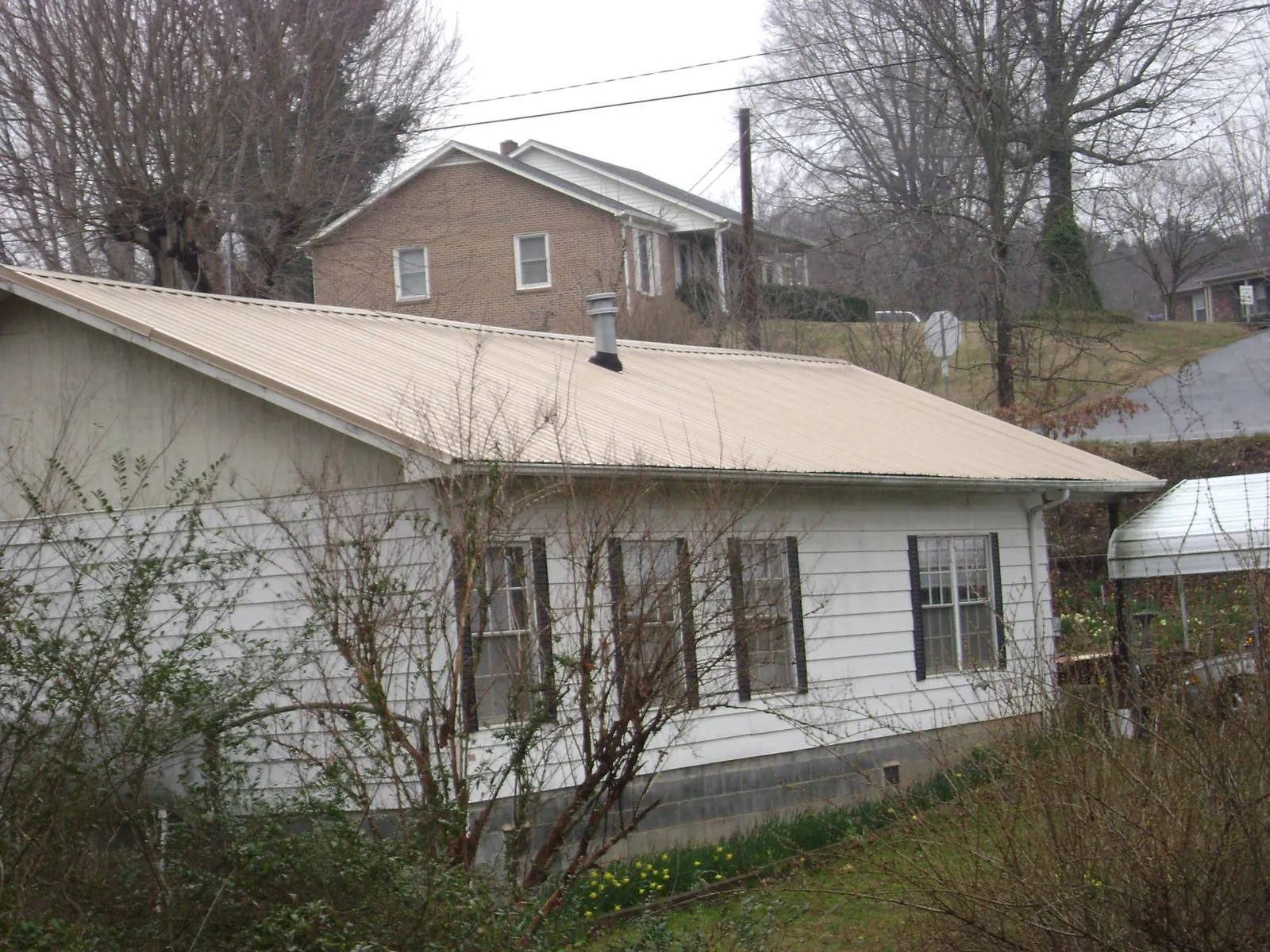Tan metal roof on a white sided house set into a hillside — Commercial Roofing by Roofing Brothers in Westfield Center
